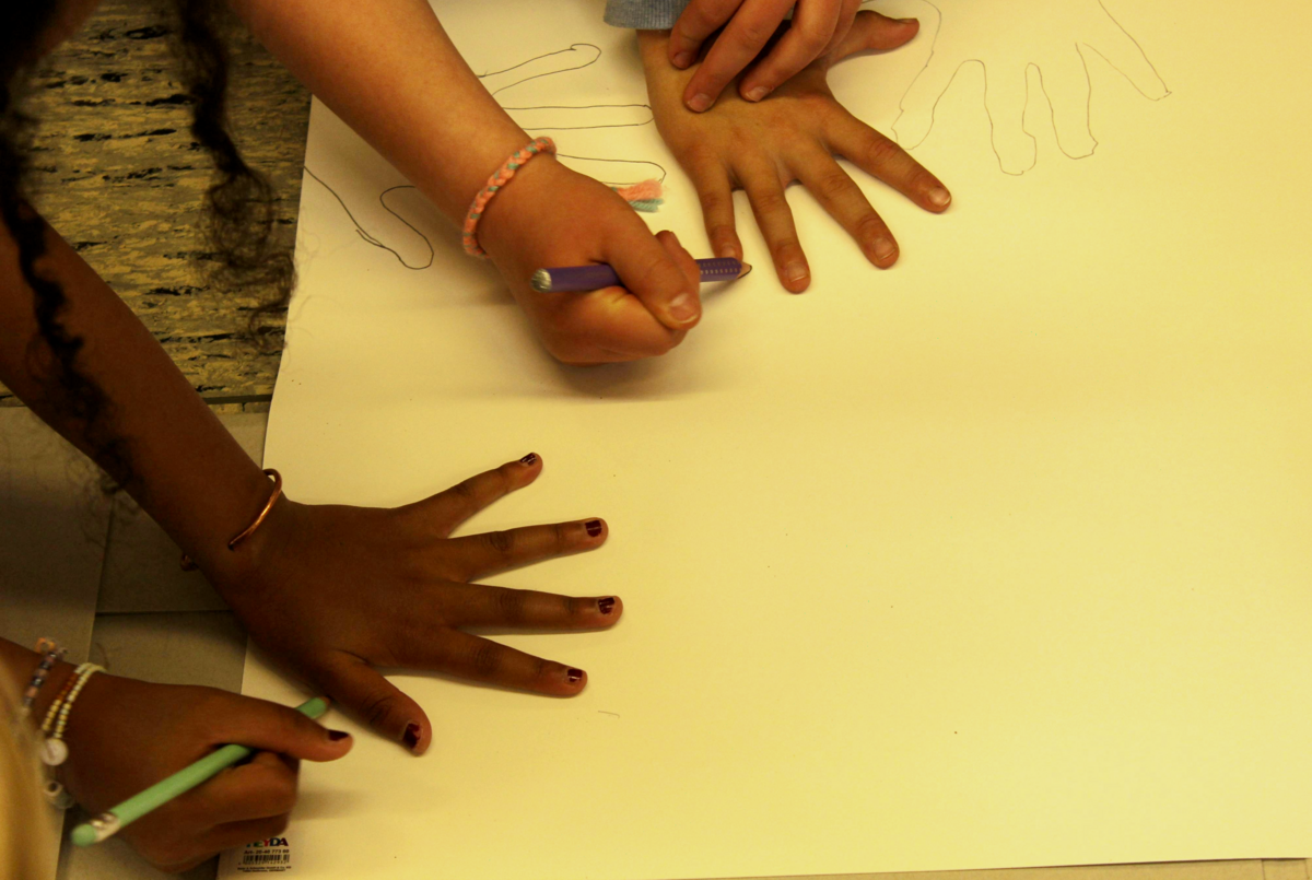 Kinder umranden ihre Hände mit einem Stift und erzeugen so auf einem Blatt Papier ihren Handabdruck